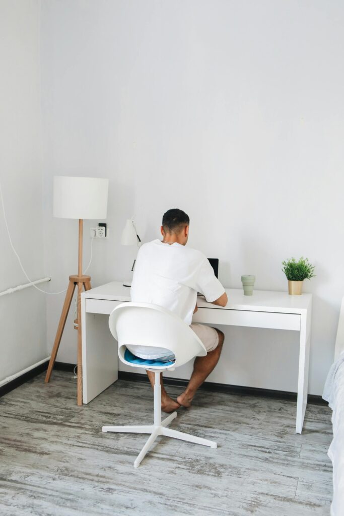 Adult male sitting at a desk studying online in a bright, minimalist room.